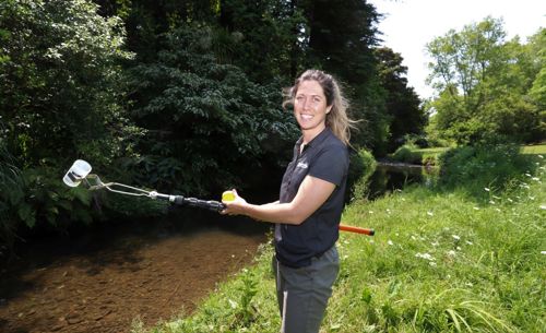 Monitoring Officer with water sampling pole by a stream.