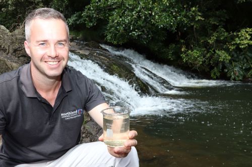 Man holding water sample beside Raumanga Falls.
